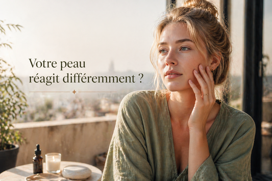 Femme en lumière naturelle sur une terrasse touchant son visage, illustrant une peau qui réagit différemment aux soins selon son état