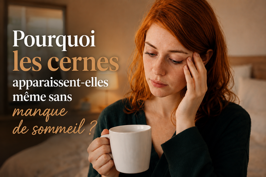 Femme rousse tenant une tasse dans une chambre chaleureuse, regard marqué par des cernes malgré une bonne nuit de sommeil, illustration éditoriale Bellasteria sur les causes des cernes sans fatigue apparente.